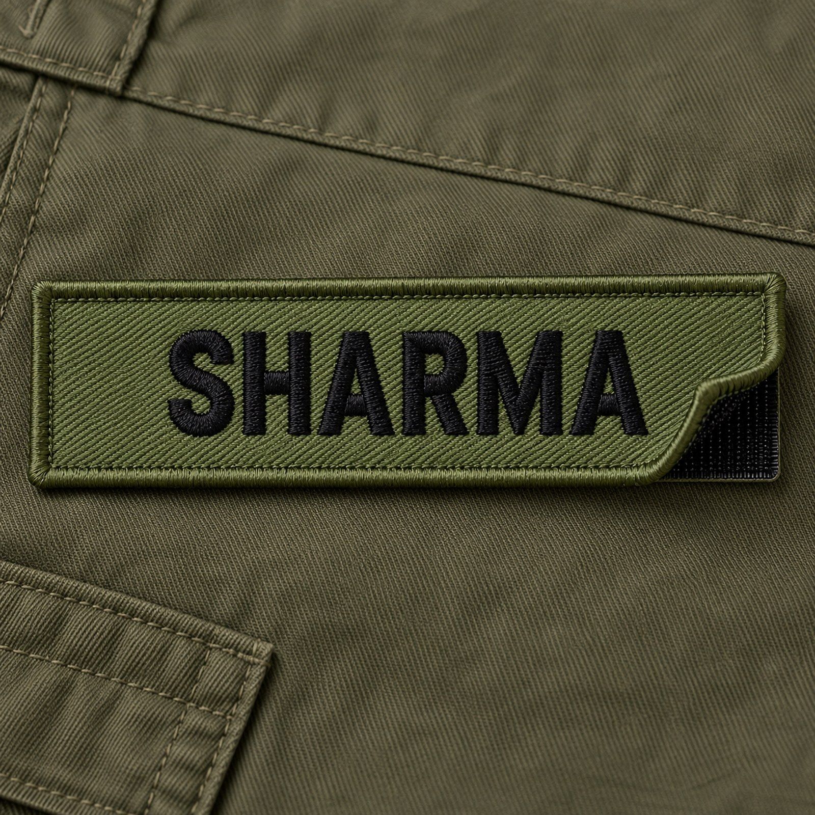 Embroidered velcro name tab stitched in green with black lettering, laid on combat uniform fabric